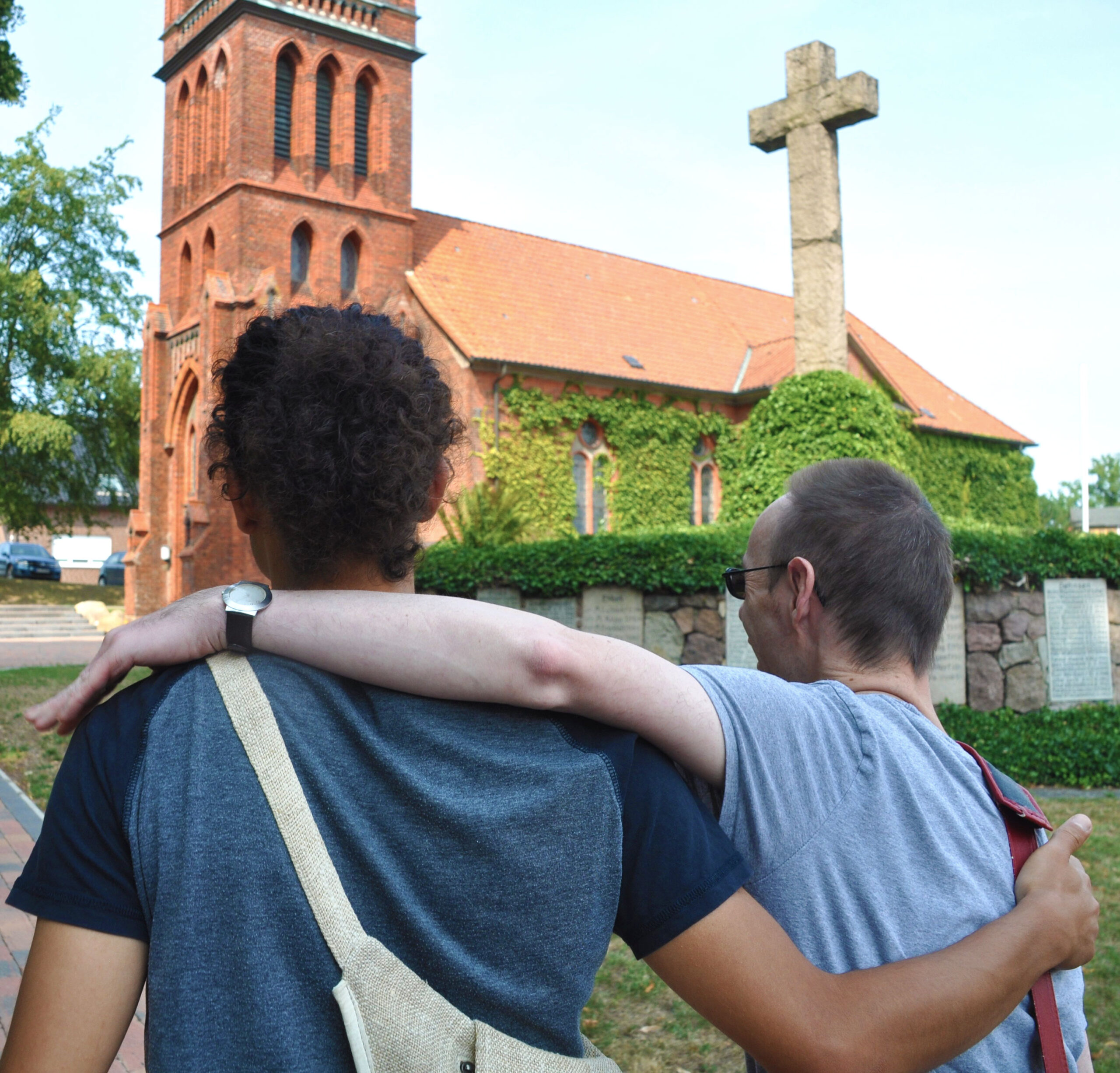 Zwei Männer stehen Arm in Arm vor einer Kirche